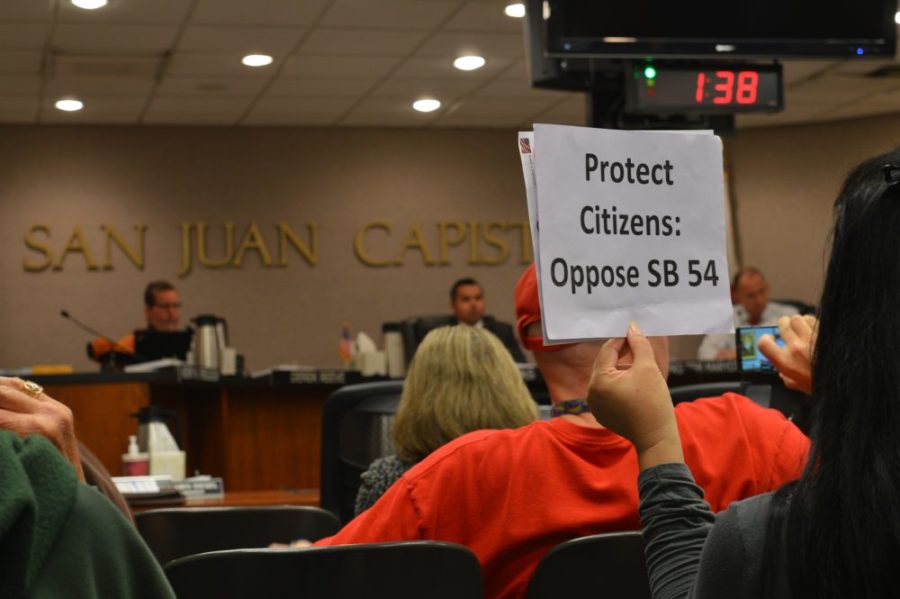 A supporter of the symbolic resolution against Senate Bill 54, this woman holds a sign showing her disagreement with the bill. The city council in the distance, listening to the public and what they have to say. 