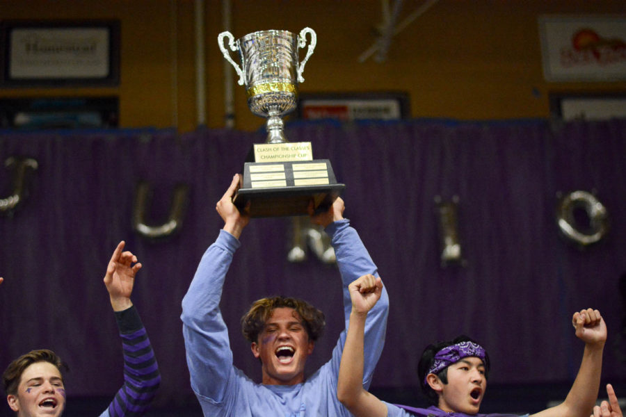 Junior, Austin Shreeve, holds up the trophy after his class wins. He is alongside juniors Cooper Kitaen and Ian Fu who are all standing in front of a crowd of excited juniors.
