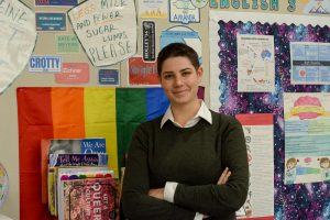 Danielle Serio poses in front of a section of her LGBTQ+ library of books she is curating. Serio hopes to make LGBTQ+ members at school feel more included by having this library and by distributing various LGBTQ+ flags to teachers around teachers.