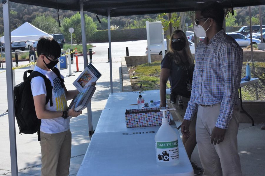 A student checks out his new textbook for the 2020-2021 school year. During textbook distribution, students and staff were required to wear masks and be socially distant from one another.