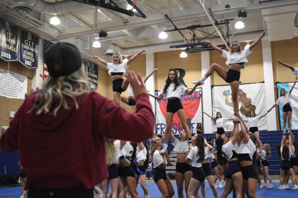 Attentively coaching the cheer team, Katie Pender helps prepare the team for the Homecoming Pep Rally. Varsity cheerleaders, Kate Warezak (12), Sidney Campbell (11), and Kennedy Canizales (12) practice making a V-like formation in preparation for the rally. 