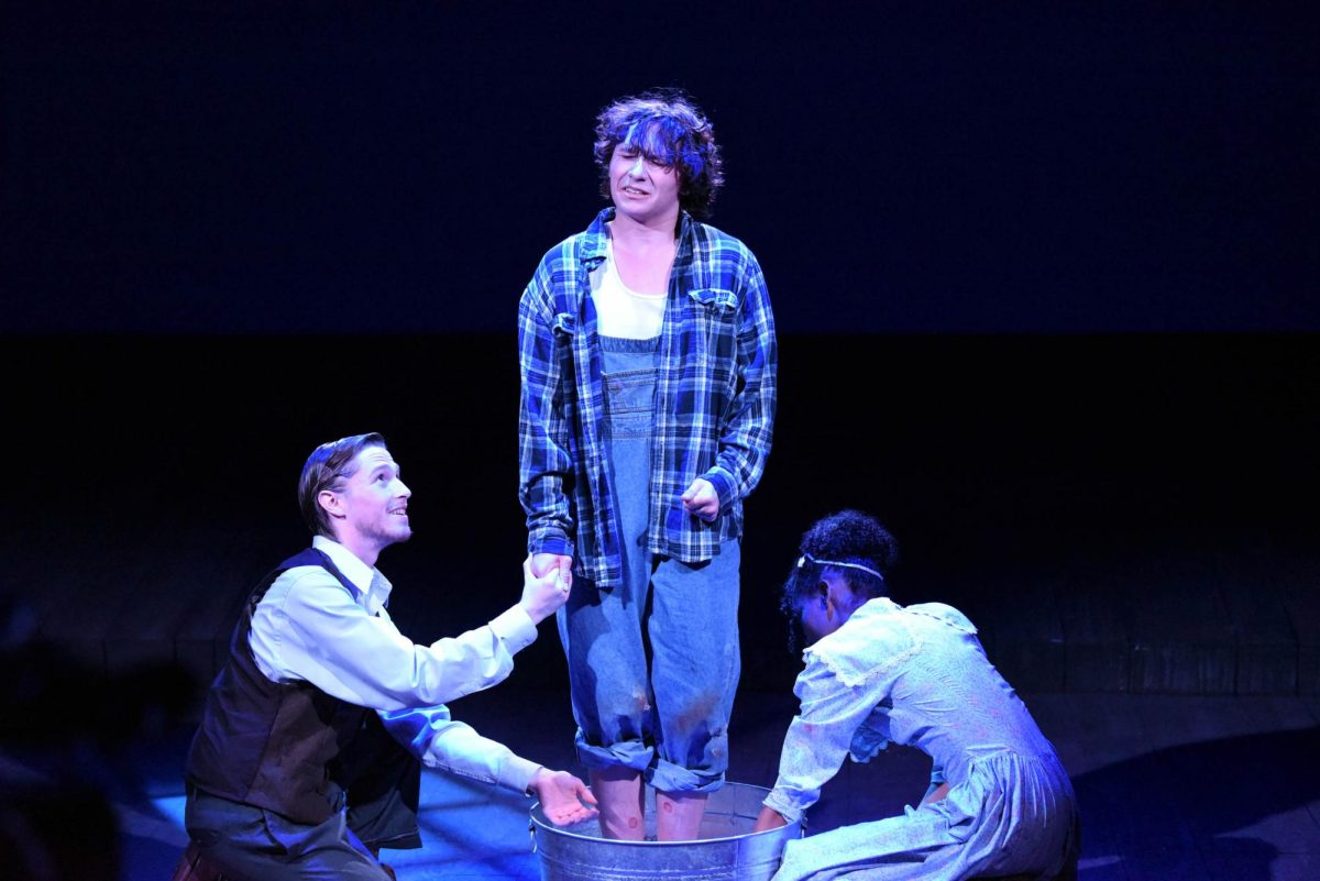 C.C. Showers, Jacob Koclanis (12), and Jennie Mae Layman, Emery Thompson (10), attempt to rid mentally challenged Buddy Layman, Leo Perry (11), of his ringworm by washing his feet with warm water. Throughout the entirety of the play, the main characters try to relieve Buddy of his uncomfortable infection, but this task proves to be difficult as Buddy is unwilling to go anywhere near water after his own mother drowned.