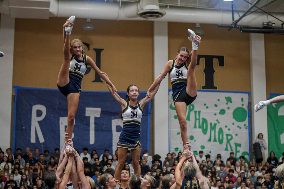 Hyping up the crowd, Varsity cheerleaders Elle Gajda (11), Greta Wolfsohn (12), and Reese Gajda (12) show off their impressive athleticism. Posing in their pyramid stunt, the Gajda sisters show off their heel stretches while Wolfsohn braces as center flyer. 