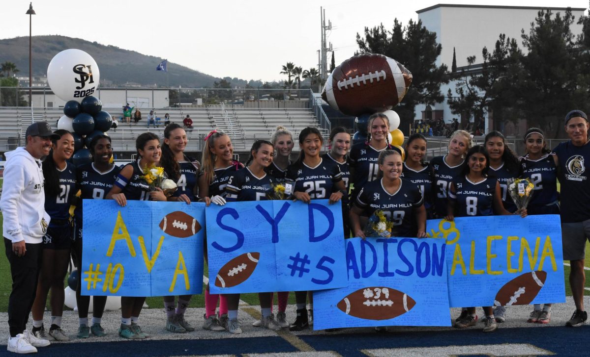 The varsity flag football players stand together in smiles, surrounding the seniors for senior night. The seniors hold the posters made by their teammates with heart-felt messages written on them. These athletes stay undefeated and won this game against Dana Hills 38-0.