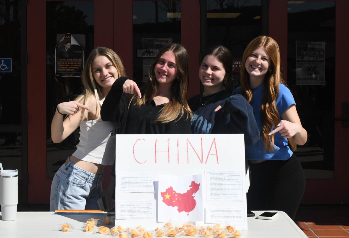 Gianna Elkins (12), Reese Gajda (12), Emilie Luzuriaga (12), and Maddy Shwam (12) pose in front of their table during multicultural fair, promoting chinese culture and one of their signature sweet treats, the fortune cookie.