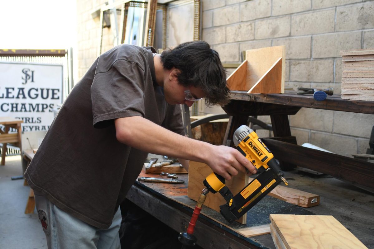 August Lind (12) uses a nail gun to complete his BITA project. In this class, students are taught how to safely use tools to construct various projects. 