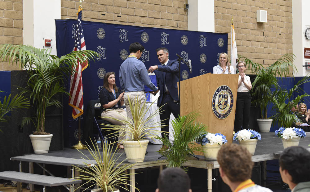 Graduating Seniors and their families come together for the San Juan Hills High School award ceremony, where lucky students get awarded for their academic and moral excellence. Principal, Cina Abedzadeh  awards Evan Lau for having the best grade point average in his senior class, Alexandra Easton, Trustees Lisa Zollinger and Gila Jones all clap and celebrate Lau’s success.  
