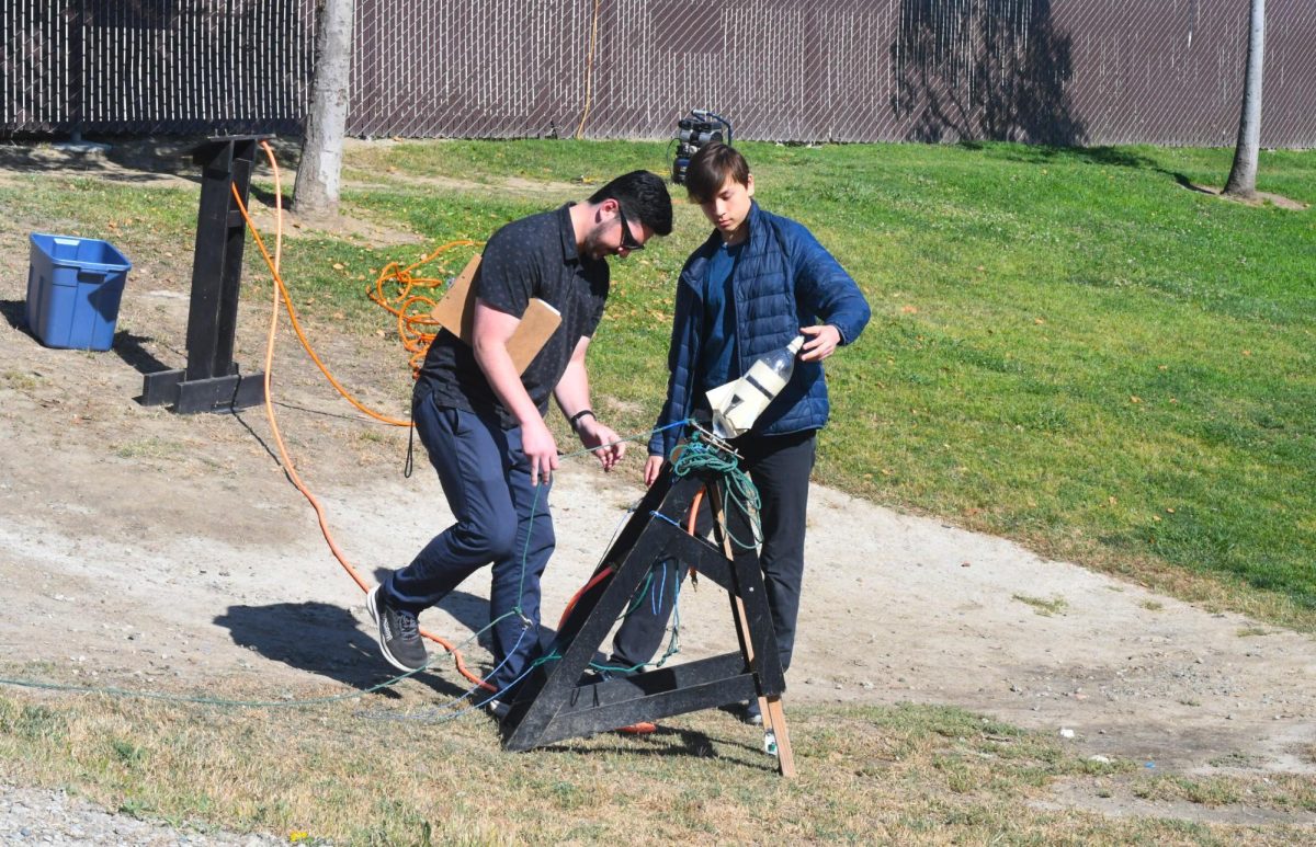  Alongside assistant teacher Mr. Anderson, physics student Connor Leycauf (11) sets up his self-made bottle rocket as one of his final projects of the year. Physics classes are instructed to build rockets out of 1L bottles to demonstrate multiple laws of physics and pressurization.