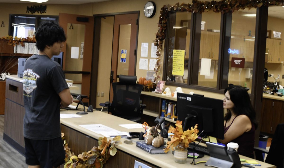 A student exchanges Chromebook in the library. Currently it is staffed by substitute librarians.