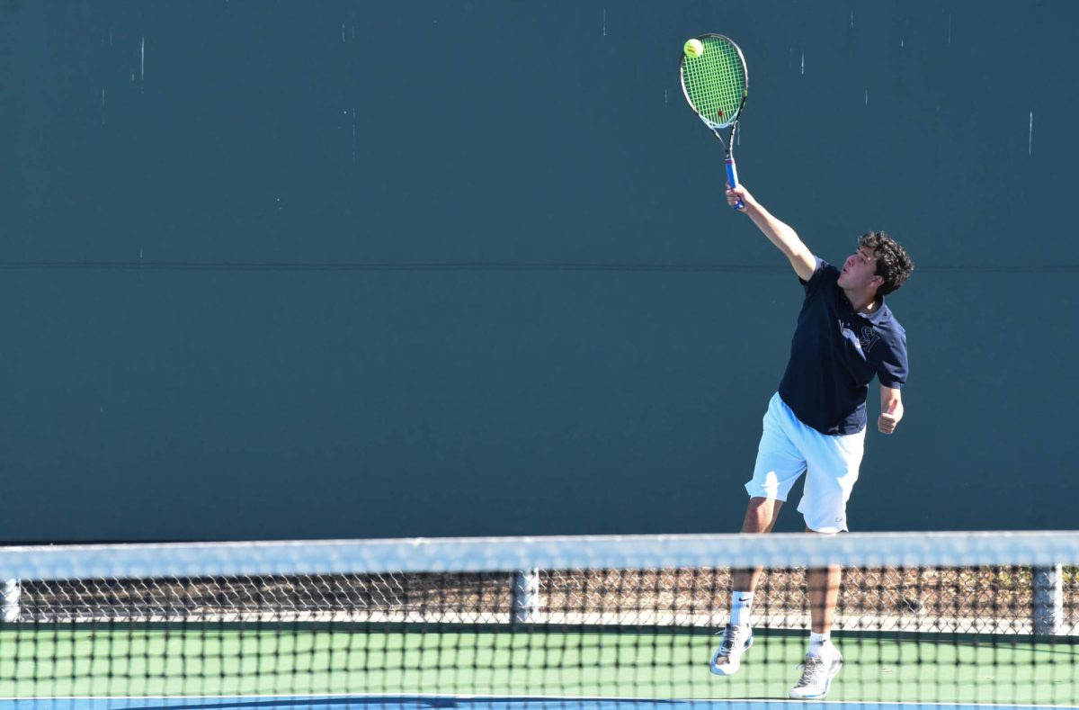James Crow (11) reaches up to serve the ball, starting the point during a single’s match against Aliso Niguel. He led the score with 2-1.