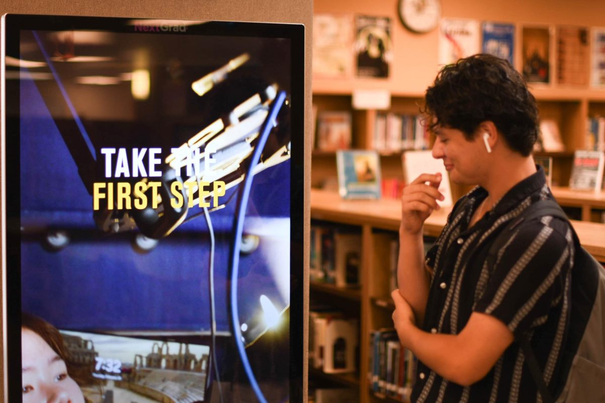 Pictured is Sammy Clementino (12), seen reading the new screen in the library. This screen promotes helpful information for students as well about different topics and things going on around campus. The screen was installed recently and adds new life to the library. 