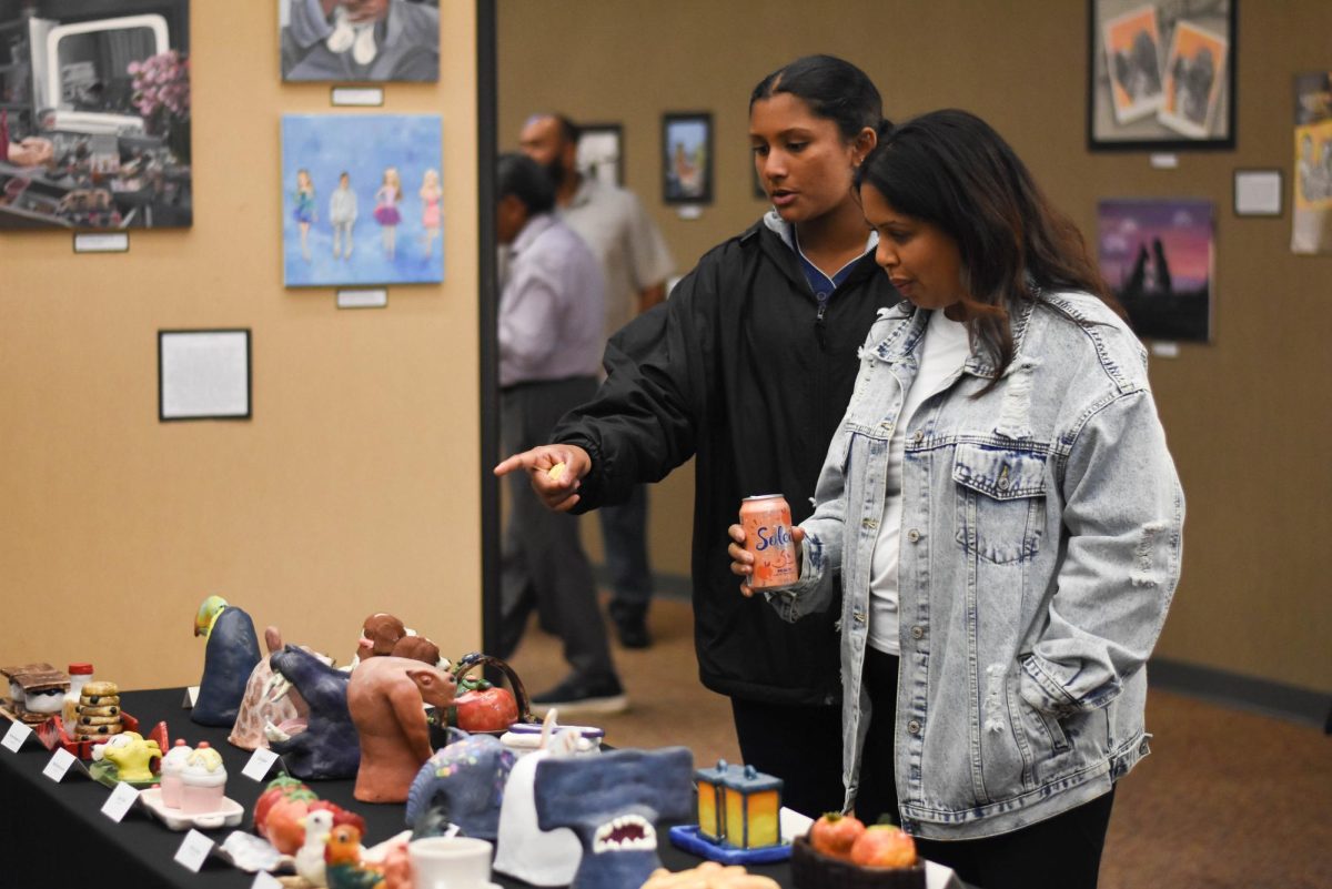 Two family members pause at the ceramics display, taking in the pieces and exchanging thoughts as they look more closely. The work sparks conversation and draws in viewers with the detail and creativity behind each piece.